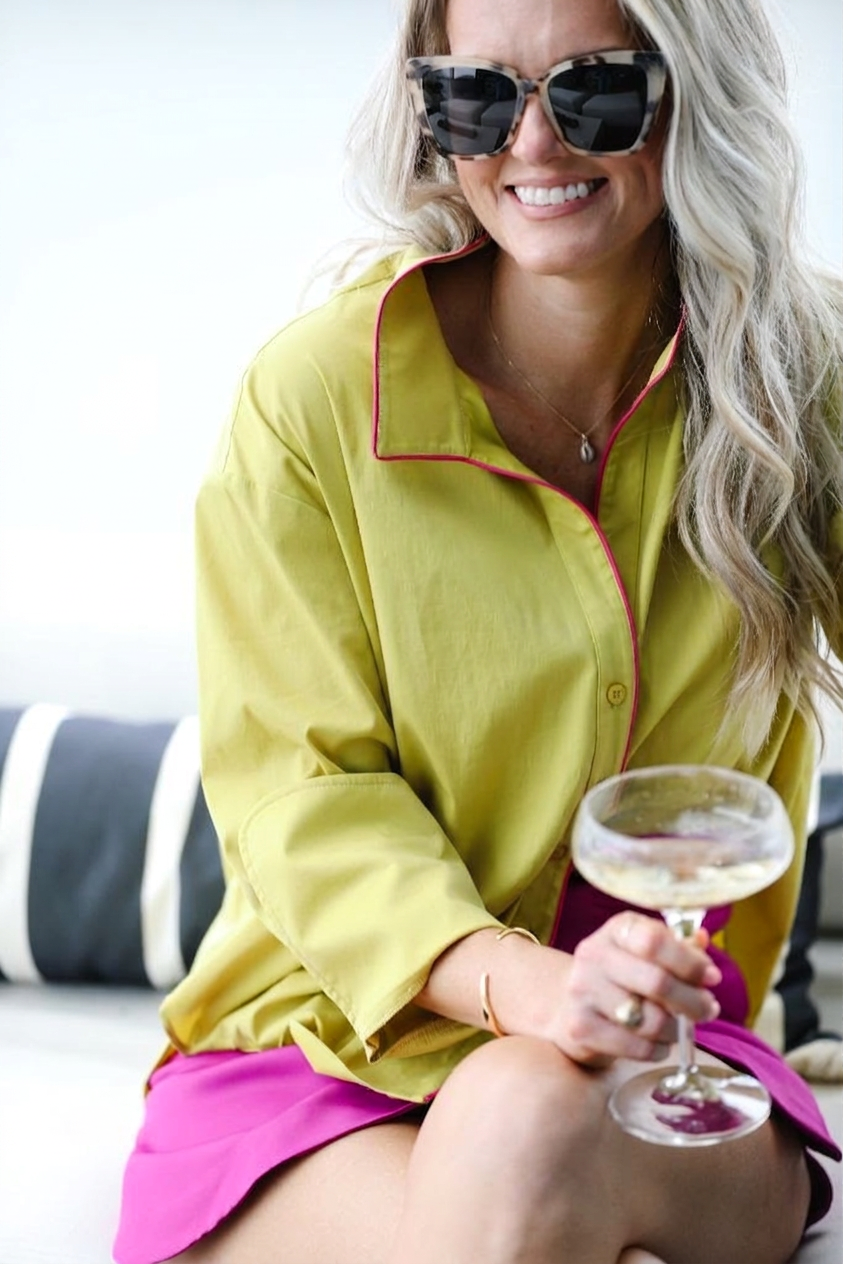 Woman in a yellow shirt with pink trim holding a glass of wine.
