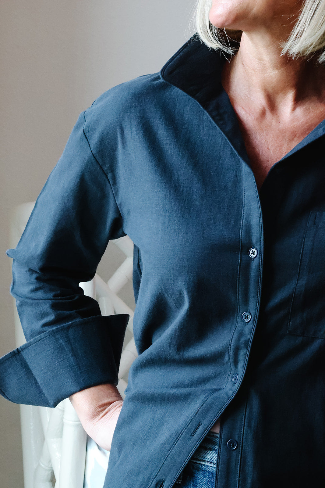 A close-up of a person wearing a dark navy blue button-up shirt with a spread collar and rolled-up sleeves, paired with blue jeans.
