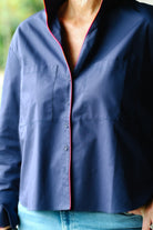 A close-up of a person wearing a navy blue button-up shirt with a contrasting pink inner placket and collar lining, paired with light blue jeans.