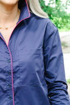 A close-up of a navy blue long-sleeve button-up shirt with bright pink piping trim along the collar, placket, and pocket, worn by a model outdoors.